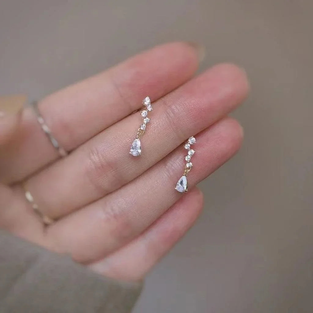 Elegant gold drop earrings with pear-cut crystals and diamond accents, held in hand