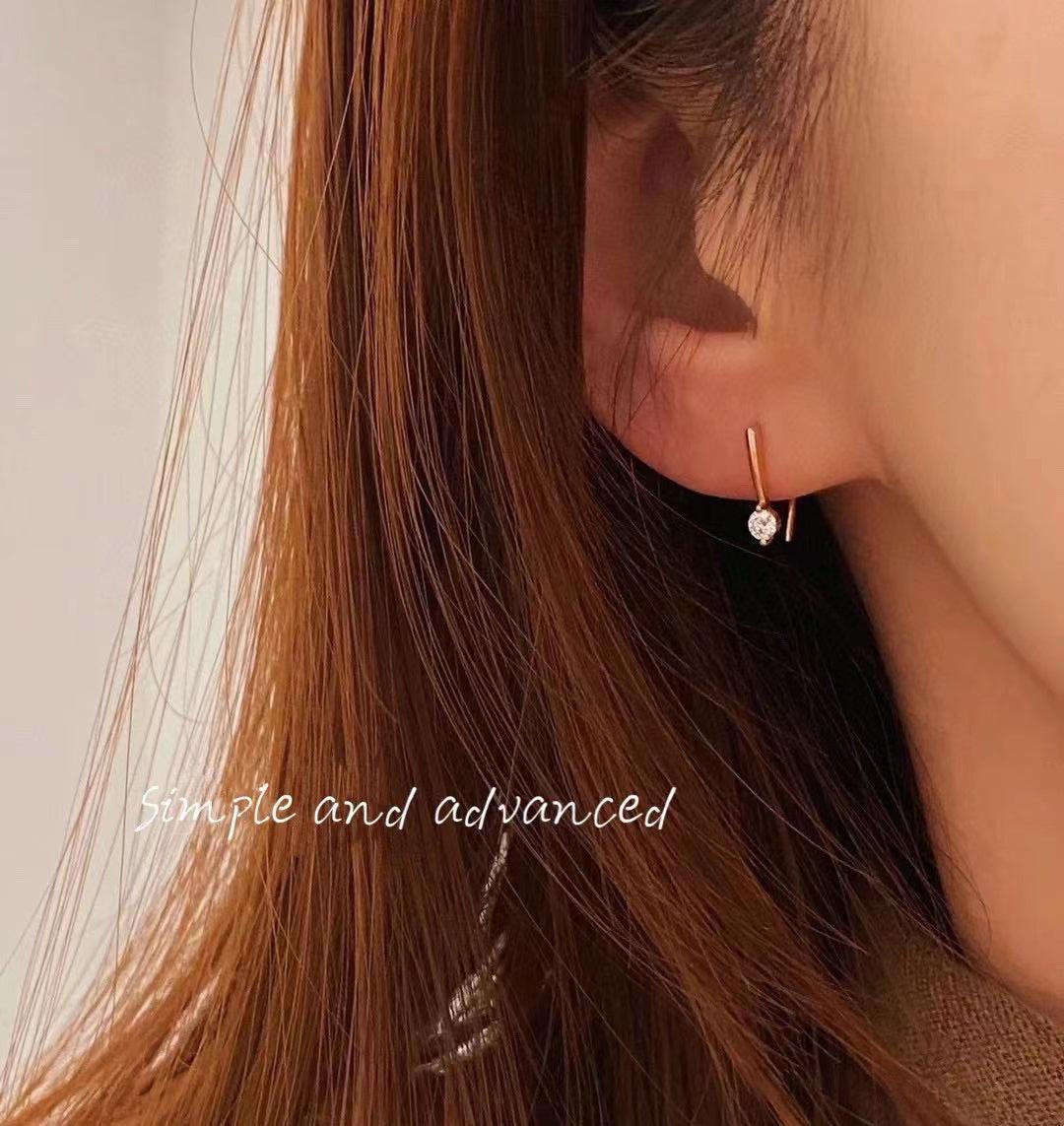Delicate gold hoop earring with heart-shaped diamond, worn by woman with long brown hair