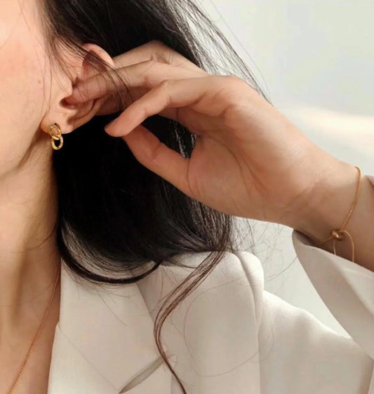 Gold interlocking hoop earrings and delicate bracelet worn by woman in white blouse