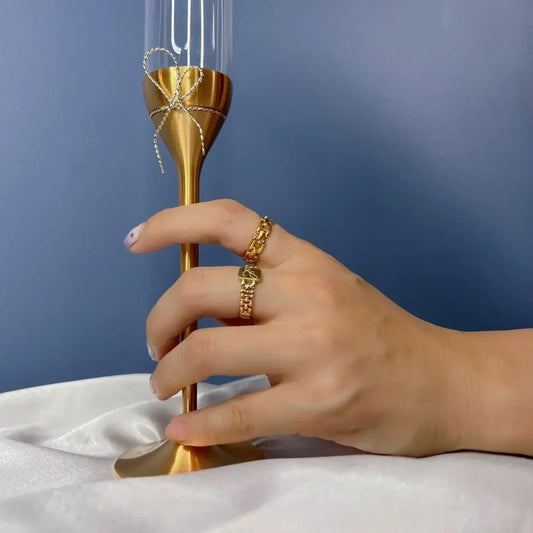 Gold chain rings on hand holding champagne flute with bow, luxury jewellery styling
