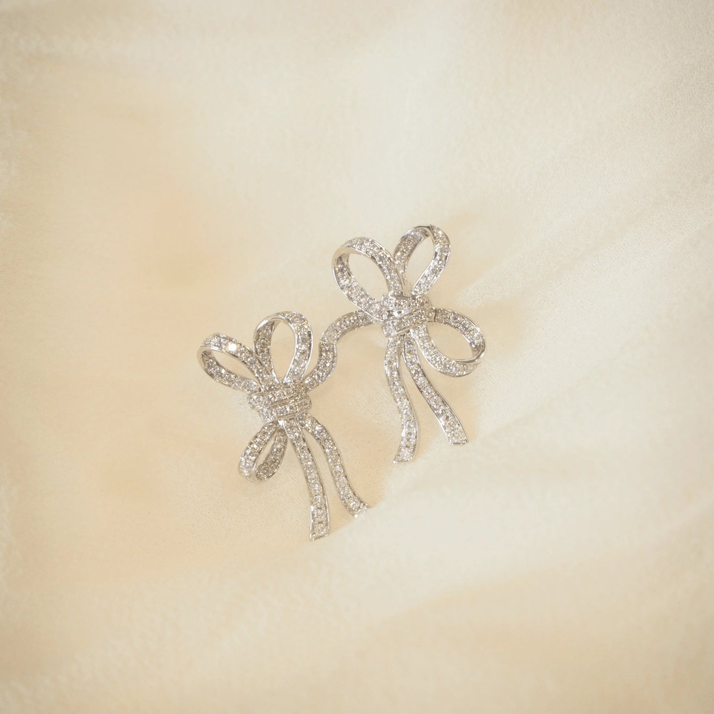 Elegant diamond bow earrings, sparkling with brilliance on soft fabric, perfect for luxury Sydney jewellery lovers.