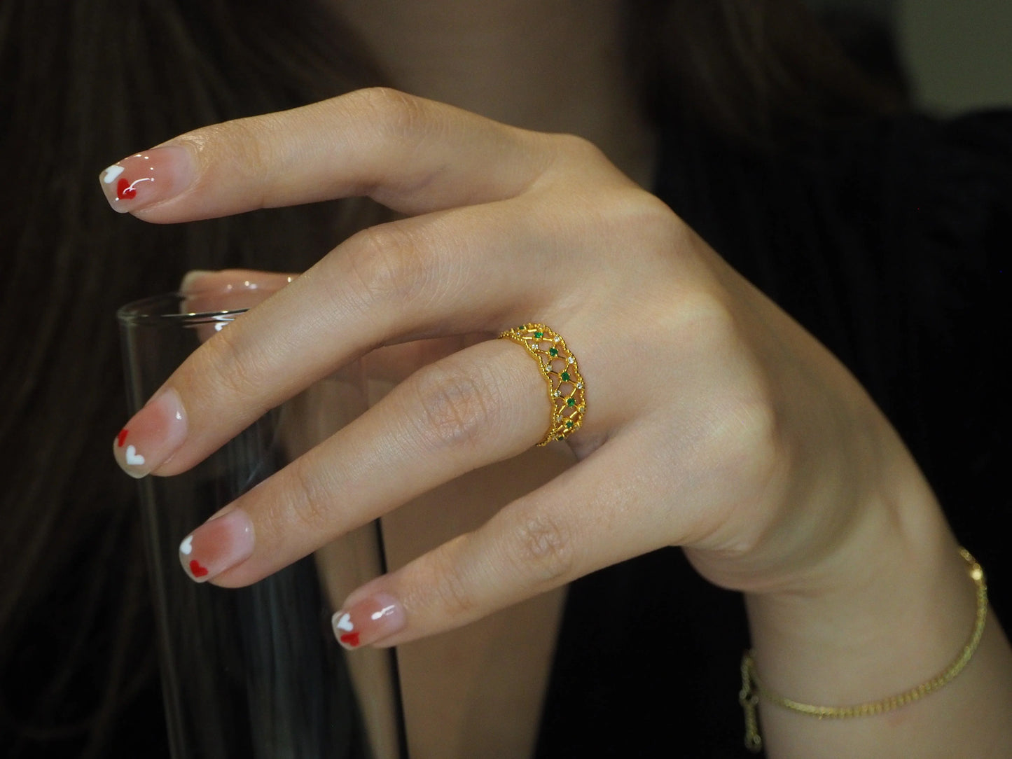 Gold ring with emerald and diamond accents on woman's hand with heart nail art